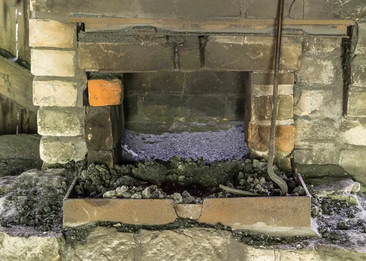 Colour photo of brick coke or solid forge with a rusted metal enclosure containing blackened coke.
