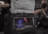 Colour photo of propane or gas forge being used by an artist blacksmith student. Inside the forge a blue and orange flame is visible. 