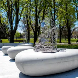 Colour photo of artist Geordie Lishman's art installation called Live. The sculpture sits on a base outside surrounded by trees.