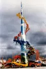 Colour photo of Bill Lishman's metal sculpture Transcending the Traffic. A tall metal cone sits in the middle of the sculpture and various small figures riding cars and bicycles made out of metal surround it.