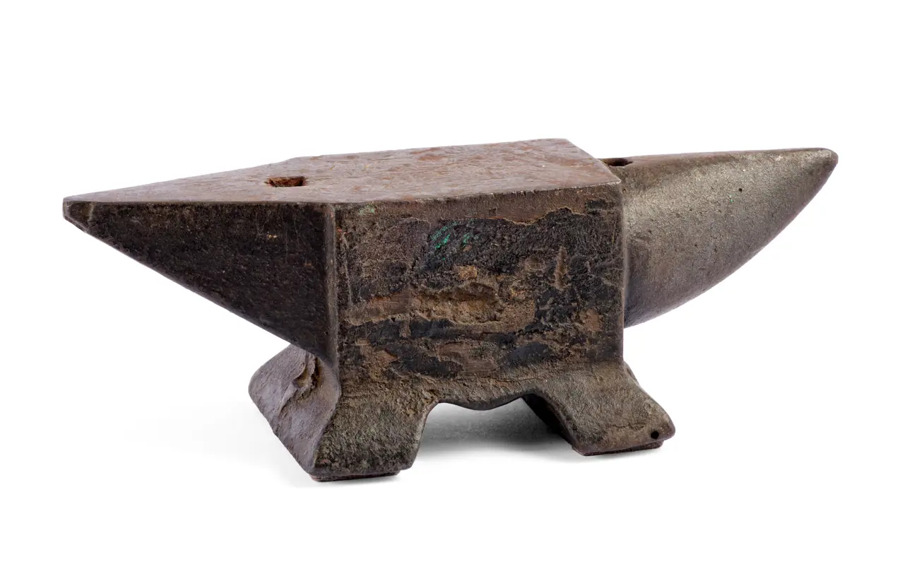Colour photo of a rusted metal European style anvil. One end extends into a point and the other end had a horn shaped extension. 