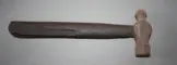 Colour photo of a rusted ball-peen hammer with a wooden handle. One end of the hammer is shaped like a ball, while the other end is flat. The hammer rests on a concrete floor.
